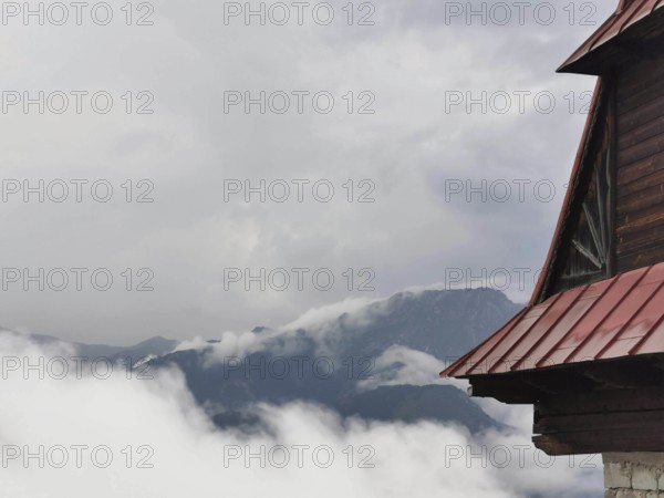 View of a mountain peak through clouds, with part of a wooden building in the foreground, Zakopane, hiking in the High Tatras National Park, Carpathian Mountains, Poland