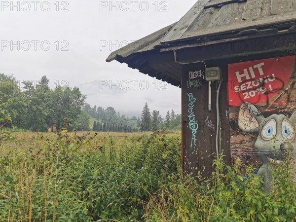 Old hut structure with poster with a cartoon mouse in the midst of a grassy landscape and cloudy sky and a mountain in the misty background, Zakopane, hiking in the High Tatras National Park, Carpathian Mountains, Poland
