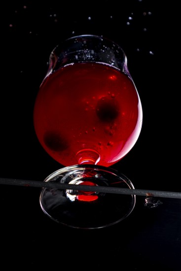 Cherries fall into a cognac glass with red liquid, dramatically illuminated, view from below