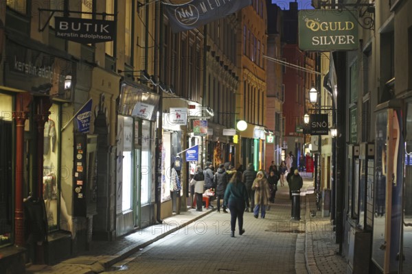 Busy street with pedestrians and illuminated shops at dusk, Gamla Stan, Old Town, Stockholm, Sweden