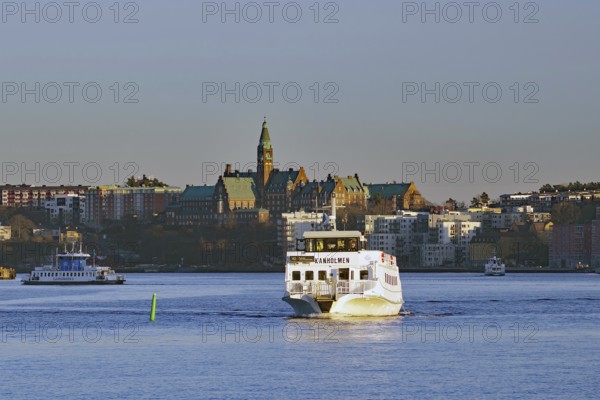 Ferry sails on a river in broad daylight with city buildings in the background, Stockholm, Sweden