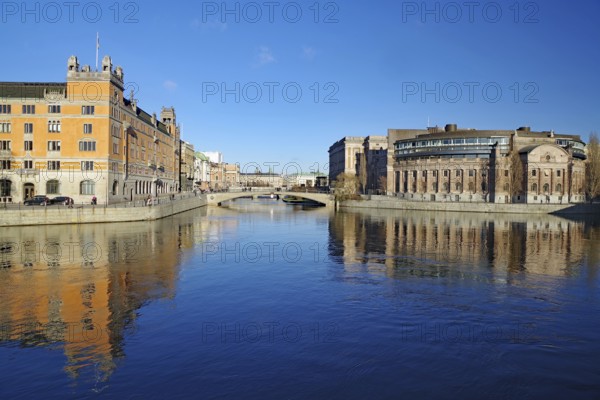 Clear river water with reflecting buildings and a bridge under a blue sky, Government District, Stockholm, Sweden