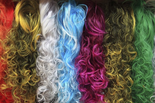 Colourful selection of long, curly wigs or hairpieces in various bright shades