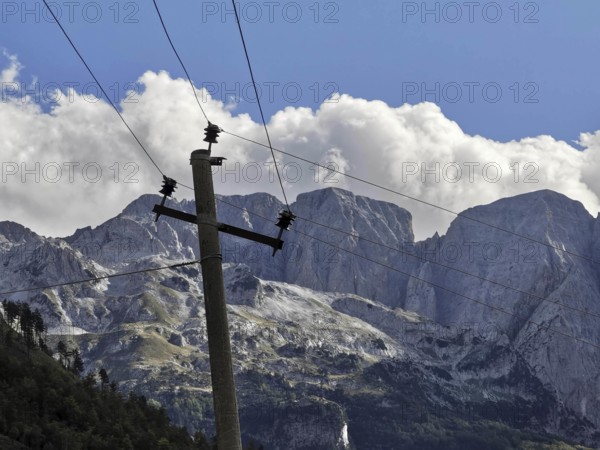 Leaning wooden power poles against rocky mountains and imposing clouds in a bright blue sky, Peaks of the Balkans, hiking in the Albanian Alps National Park, Albania