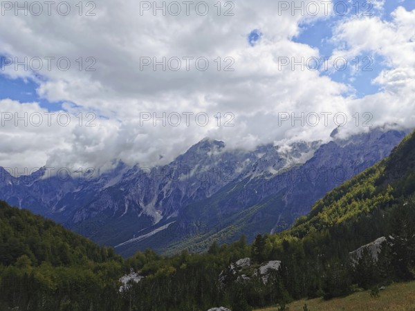 Mountain landscape with thick clouds and extensive forests in daylight, Peaks of the Balkans, hiking in the Albanian Alps National Park, Albania