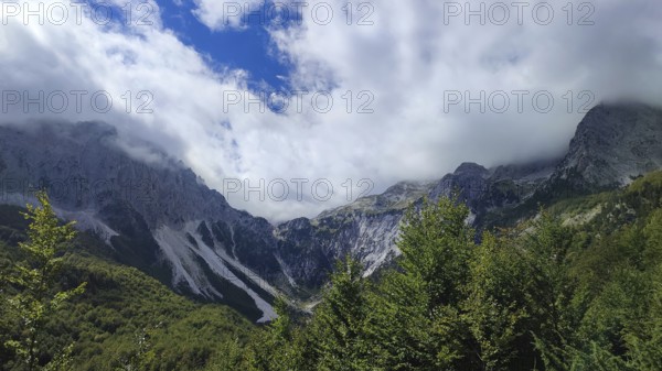 Mountain panorama, majestic mountain landscape with clouds and thick forests under blue sky, Peaks of the Balkans, hiking in the Albanian Alps National Park, Albania