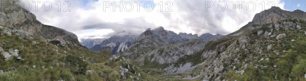 Wide mountain panorama under cloudy sky, with rocky elevations and a valley, Peaks of the Balkans, hiking in the Albanian Alps National Park, Albania, Peaks of the Balkans, hiking in the Albanian Alps National Park, Albania