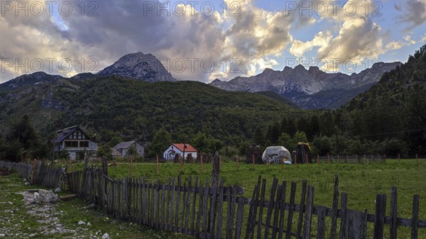 Idyllic farm against a dramatic mountain backdrop in the warm light of sunset, Peaks of the Balkans, hiking in the Albanian Alps National Park, Albania