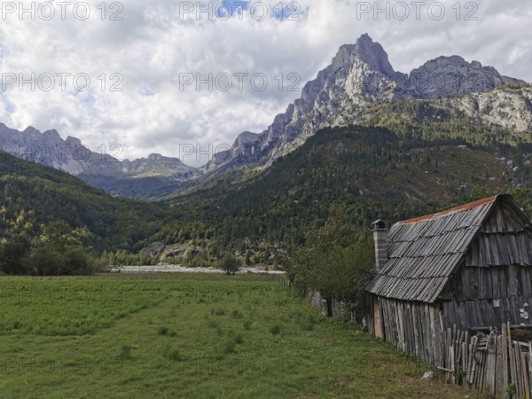 Small wooden cabin in a grassy willow with majestic mountains in the background, Peaks of the Balkans, hiking in the Albanian Alps National Park, Albania