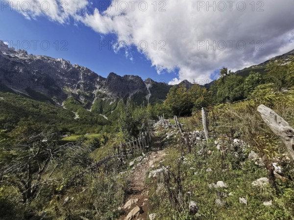 Rocky hiking trail along a hill surrounded by mountains under rugged skies, Peaks of the Balkans, hiking in the Albanian Alps National Park, Albania