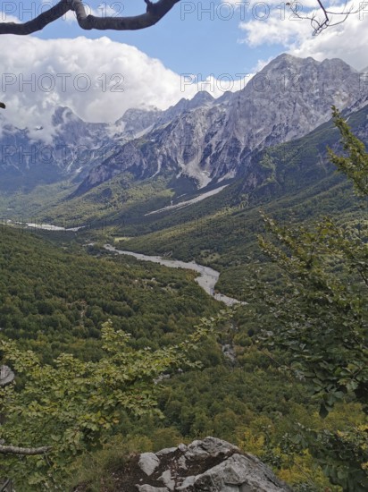 Wide view of a green valley with a river and high mountains under cloudy sky, Peaks of the Balkans, hiking in the Albanian Alps National Park, Albania