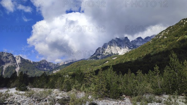 Majestic mountains with eye-catching cloud formations over dense forest, Peaks of the Balkans, hiking in the Albanian Alps National Park, Albania