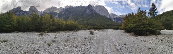 Panorama, wide riverbed in front of a wooded mountain landscape under blue sky and clouds, Peaks of the Balkans, hiking in the Albanian Alps National Park, Albania