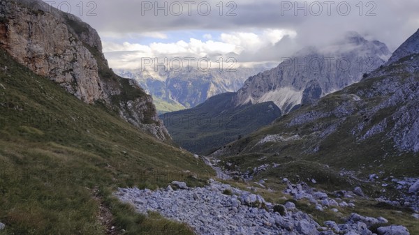 View of a rocky valley surrounded by imposing mountain ranges under a partly cloudy sky, Peaks of the Balkans, hiking in the Albanian Alps National Park, Albania