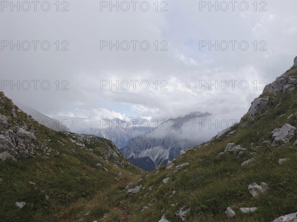 Snowy valley surrounded by mountains, partly obscured by clouds and fog, Peaks of the Balkans, hiking in the Albanian Alps National Park, Albania