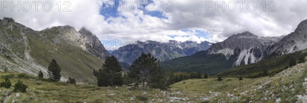 Extensive mountain panorama with forests between rocky peaks and clouds, Peaks of the Balkans, hiking in the Albanian Alps National Park, Albania