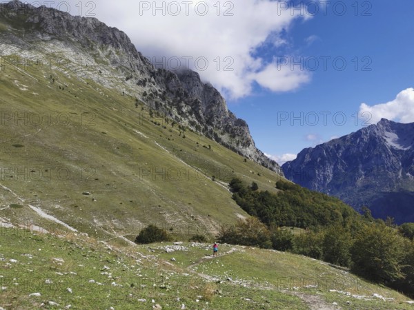Extensive alpine landscape under a cloudy sky next to imposing mountain slopes, Peaks of the Balkans, hiking in the Albanian Alps National Park, Albania