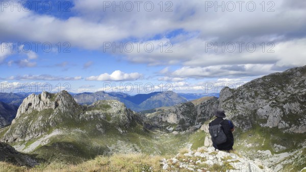 Hiker with backpack enjoying the view of a wide mountain valley under a partly cloudy sky, looking towards Kosovo and Montenegro, Peaks of the Balkans, hiking in the Albanian Alps National Park, Albania