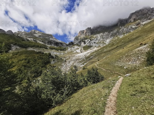 Trail through a mountainous landscape with dramatic clouds in the sky, Peaks of the Balkans, hiking in the Albanian Alps National Park, Albania