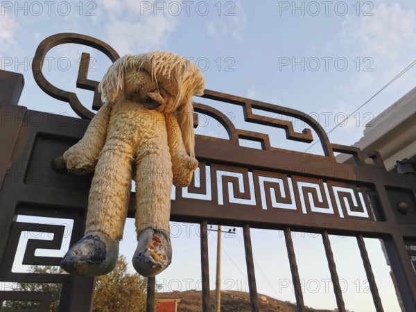 An old plush bear hangs abandoned on a rusty, metal gate at dusk, Himare, Albania
