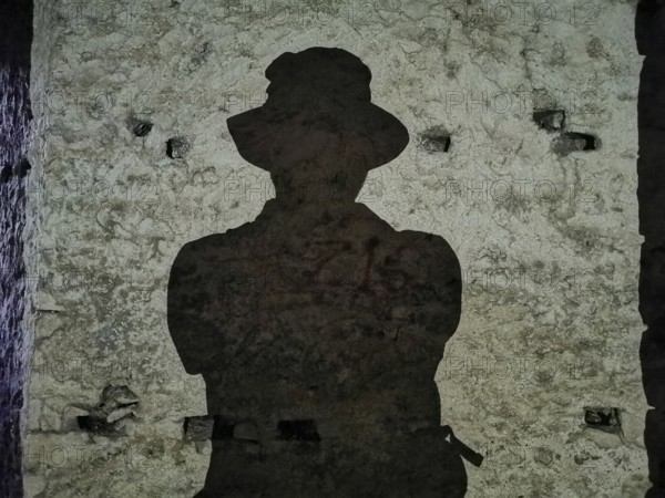 A dark shadow silhouette of a person wearing a hat on an old stone wall, Albania