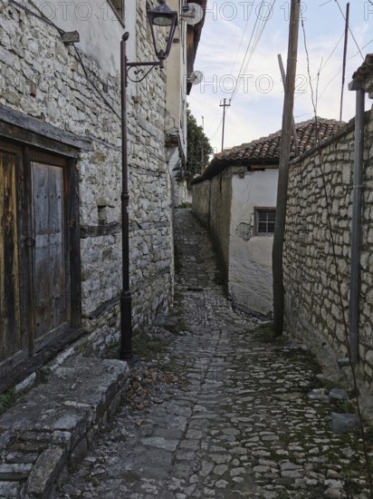 Narrow, cobblestone alley with old stone walls and traditional houses, old town of Berat, Albania