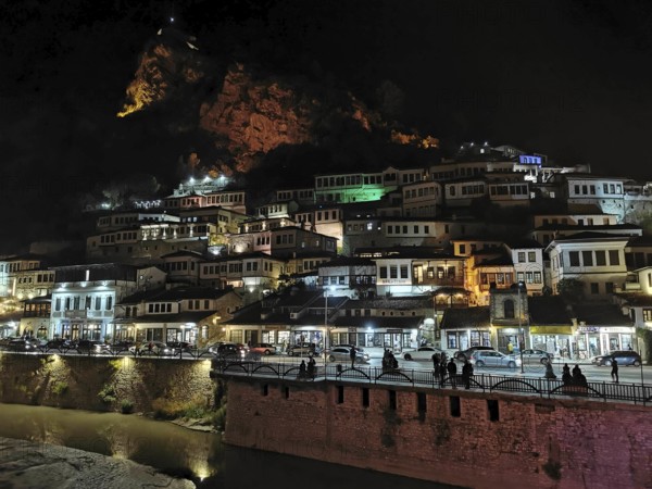 Night view of an illuminated city on the slope of a hill with river in the foreground, Berat, Albania