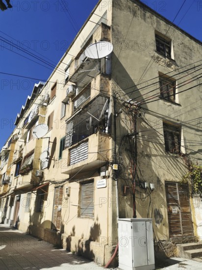 Old, yellowed building cluttered with power lines with numerous satellite dishes and cables in the city, Shkodra, Albania