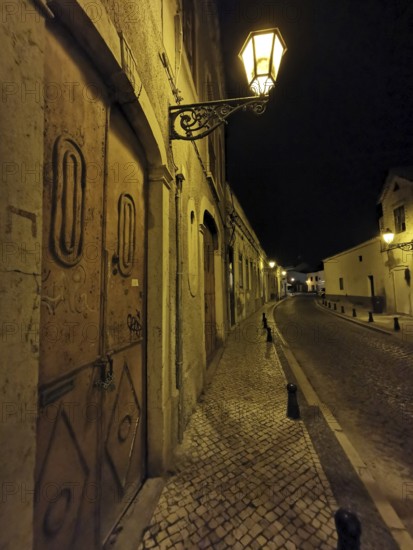 Night view of a lonely paved street with cozy glowing lanterns and historic buildings, Faro, Algarve, Portugal
