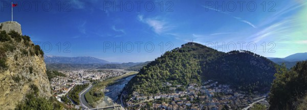 Panorama, view of a castle on a hill with Albanian flag with river and city in the valley under a clear blue sky, Berat, Albania