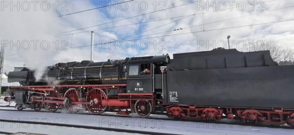 A black, historic steam locomotive emits smoke and stands on snow-covered tracks in winter, Rennsteig, Frankenwald nature park Park