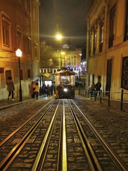 A busy scene with a tram on illuminated cobblestone streets at night, funicular, Lisbon, Portugal