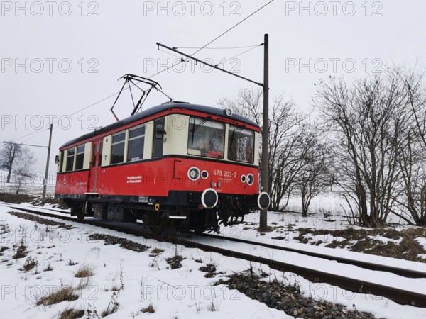 A red train moves on rails through a snowy landscape with bare trees, Bergbahn Oberweissbach, Rennsteig, Thuringian Forest nature park Park