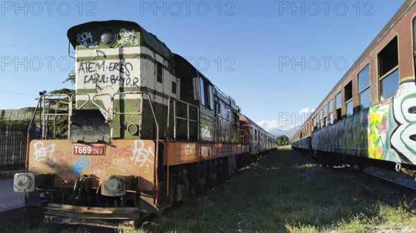Old locomotive with graffiti, on a parallel track to another train, between two trains, Albania