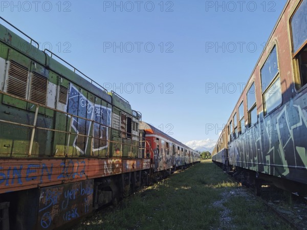 Two colorful abandoned trains full of graffiti under clear skies, Tunnelblick, Albania