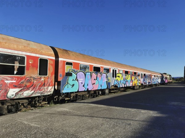 Long train with colorful graffiti on rails, blue sky above, former German railway, Shkodra, Albania