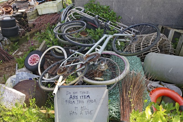 Old bikes and various objects lie messy in a garden with a warning sign, scrap collection, St Agnes, Isles of Scilly, Cornwall, Great Britain
