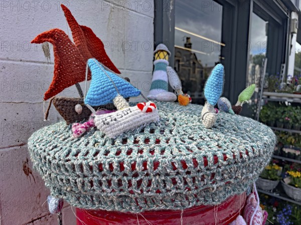 Colourful crocheted motifs of ships and houses on a wall in a maritime scene placed on a letterbox, Oban, Scotland, Great Britain