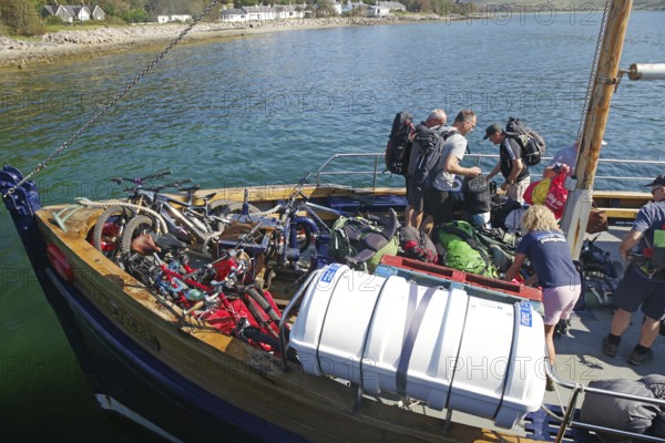 People loading a boat with bikes and luggage on a clear summer day in the harbour, Knoydart, Mallaig, Scotland, United Kingdom