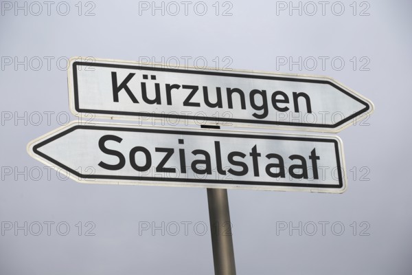 (photo montage) Directional arrows against a grey sky point in the directions of CUTS and WELFARE STATE