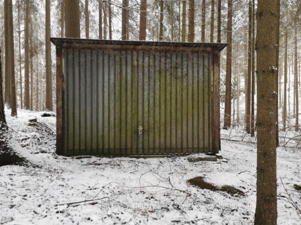 Old, mossy, rusty garage in a snow-covered forest, surrounded by tall trees, Frankenwald nature park Park