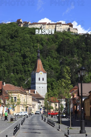 Town of Rasnov, German Rosenau. In the foreground is the distinctive clock tower of the Protestant Church, St. Matthias Church, in the background on the hill is the medieval Rasnov Fortress, Rosenau Castle, Brasov District, Transylvania, Romania