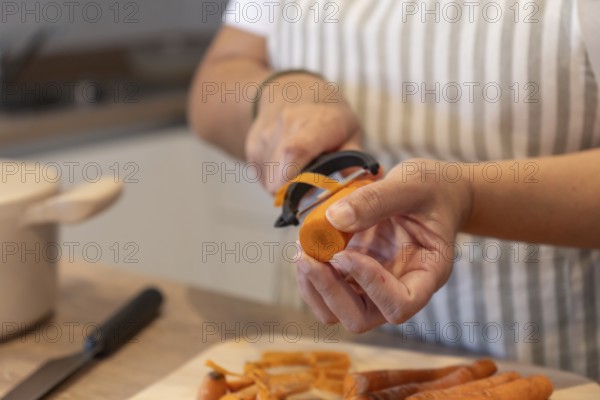 Close up of hands peeling fresh carrot in home kitchen. Healthy ingredients, simple food preparation and everyday cooking concept