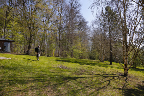 Man with backpack, meadow, bare trees, spring, Ulm University Botanical Garden, Baden-Württemberg, Germany