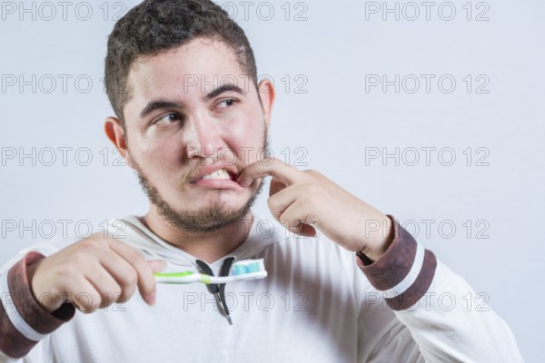 Young man with tooth sensitivity holding a toothbrush isolated. Man suffering from gum pain holding brush