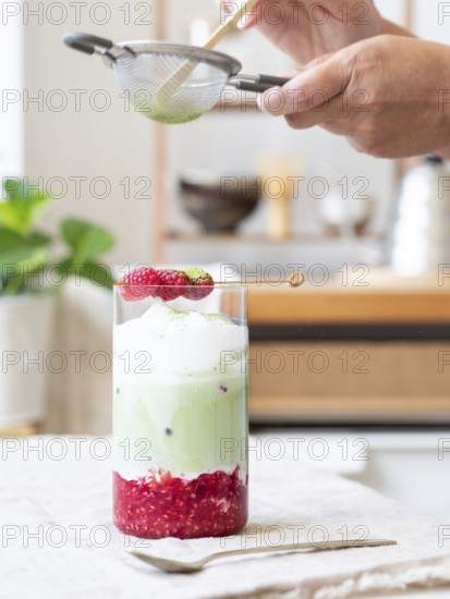 Person sifting green tea powder over a refreshing iced matcha latte with raspberries