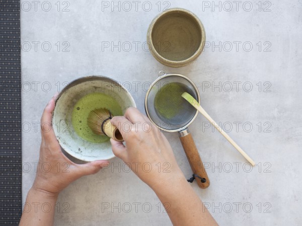 Hands whisking matcha tea in a ceramic bowl, sifting powder with a strainer