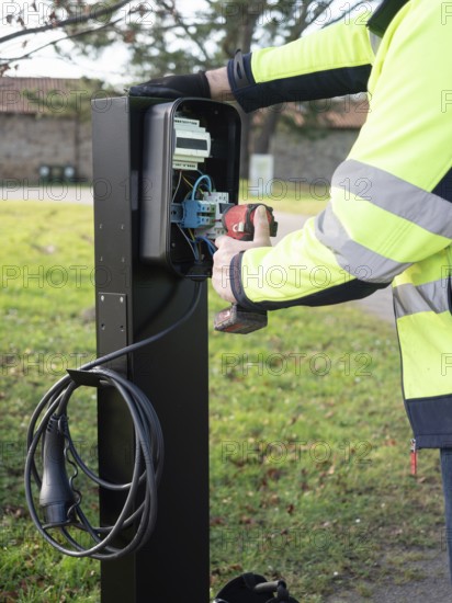 Worker installing an ev charging point, connecting wires and using a power tool for sustainable energy