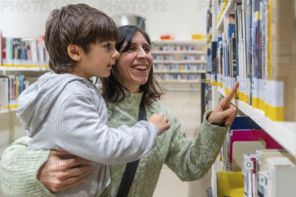 Woman and son smiling together at bookshelves, choosing a book in a library, bonding over reading and learning, showing family support, childhood literacy and education growth