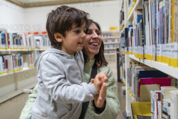 Happy mother and son enjoying a moment of discovery and learning while looking for books on shelves at a public library, promoting family education and literacy